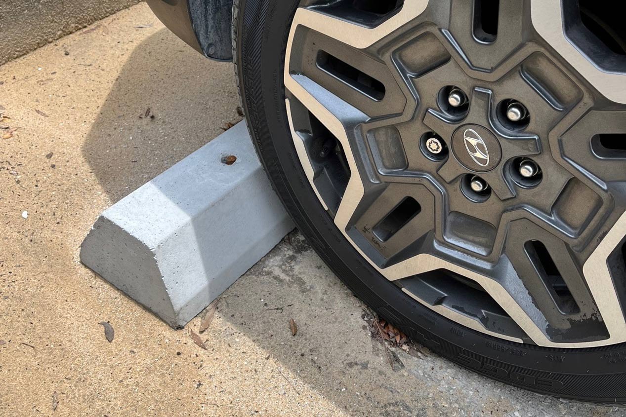 A close-up of a vehicle tire touching a wheel stop with a chamfered edge.