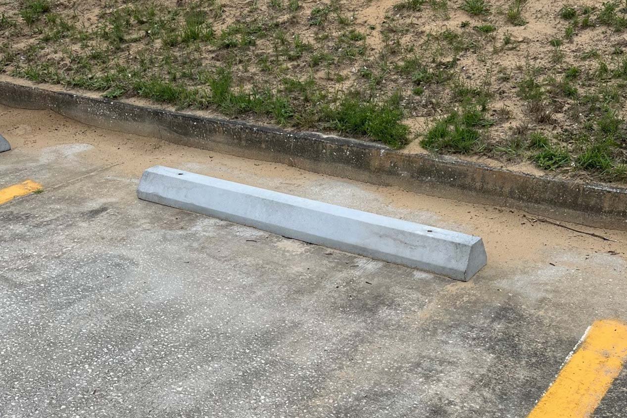 A gray precast concrete parking stop installed on an asphalt parking lot with yellow parking lot stripes. 