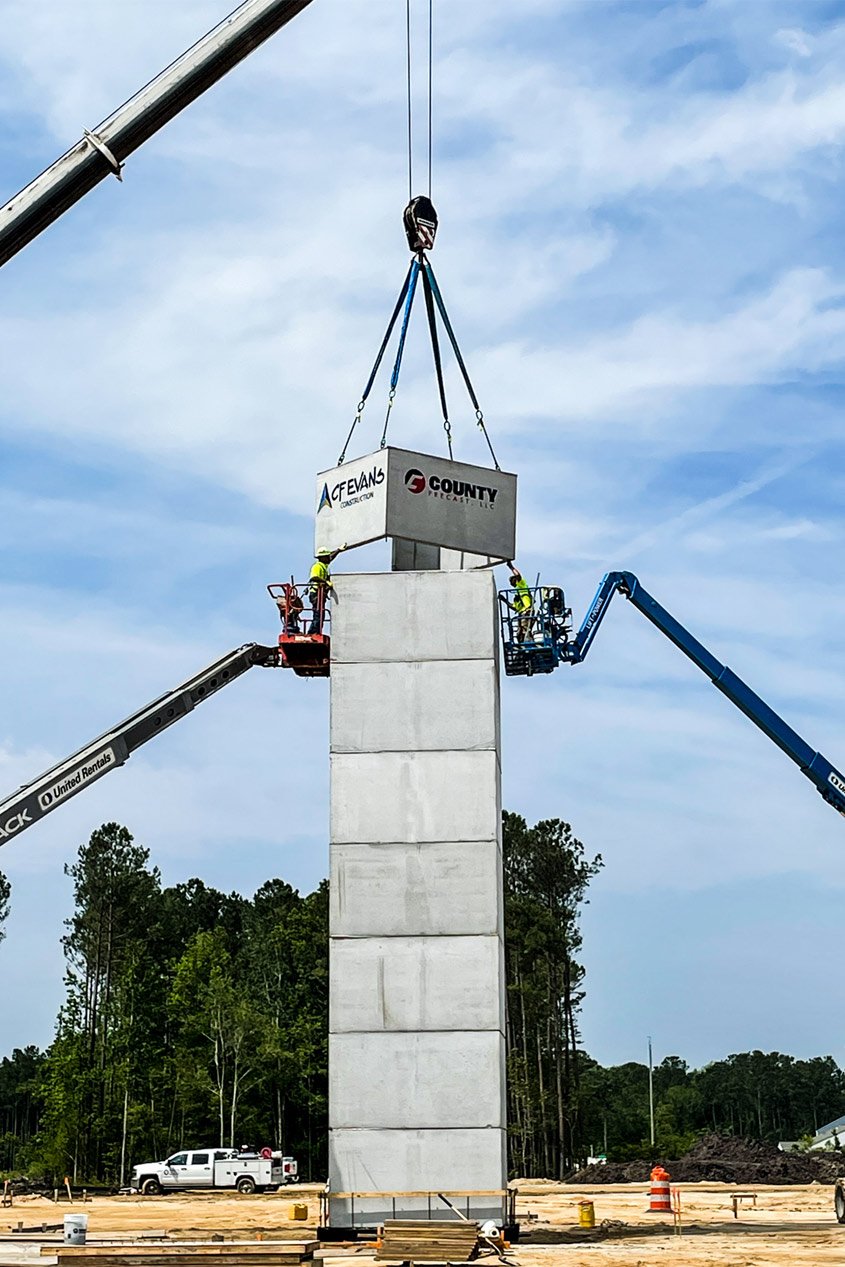 Construction workers standing on telescoping boom lifts guide a segment of a precast elevator shaft into place with the help of a crane.