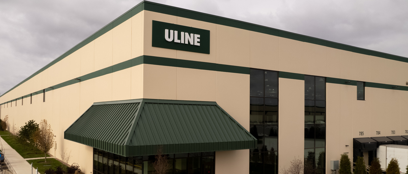 The corner entrance of a large-scale Uline distribution center, built with beige colored precast concrete panels with dark green details.